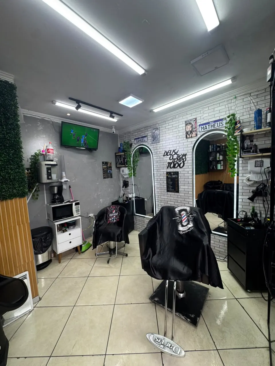Salão da barbearia com duas estações de corte, espelhos iluminados e as placas com os nomes Samuel e Matheus na parede de tijolinho