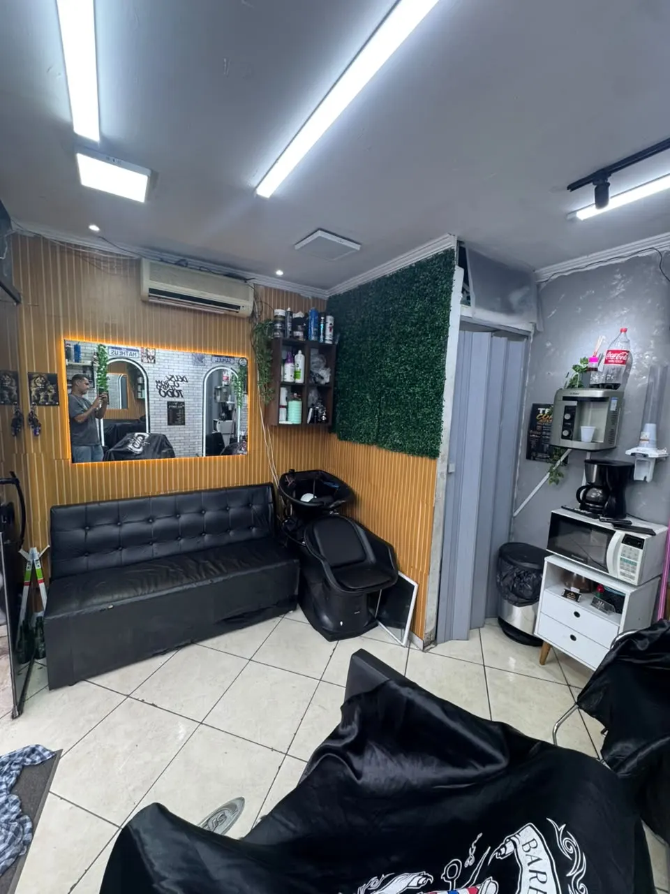 Sala de espera com sofá de couro preto e o lavatório de cabelo ao fundo